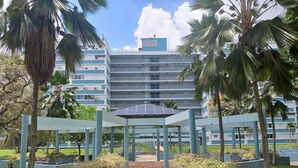 A modern building with a central atrium, surrounded by palm trees and planters. - Cozy Elegance : Tu Rincón en San Juan (San Juan)