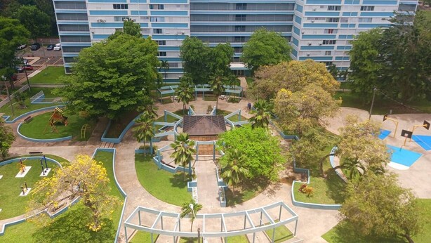 A multi-story hotel with a central courtyard featuring a playground, palm trees, and a small pool. - Cozy Elegance : Tu Rincón en San Juan (San Juan)