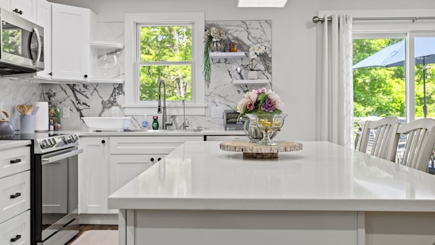 A modern kitchen with white cabinetry, a marble backsplash, and a central island with a vase of flowers.