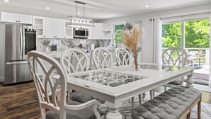 A modern kitchen with white cabinetry, stainless steel appliances, and a glass-top dining table with white chairs.