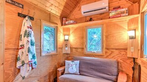 Ein gemütliches Blockhaus-Interieur mit Holzvertäfelung, einer Couch mit Kissen und zwei Fenstern mit Blick auf Bäume.