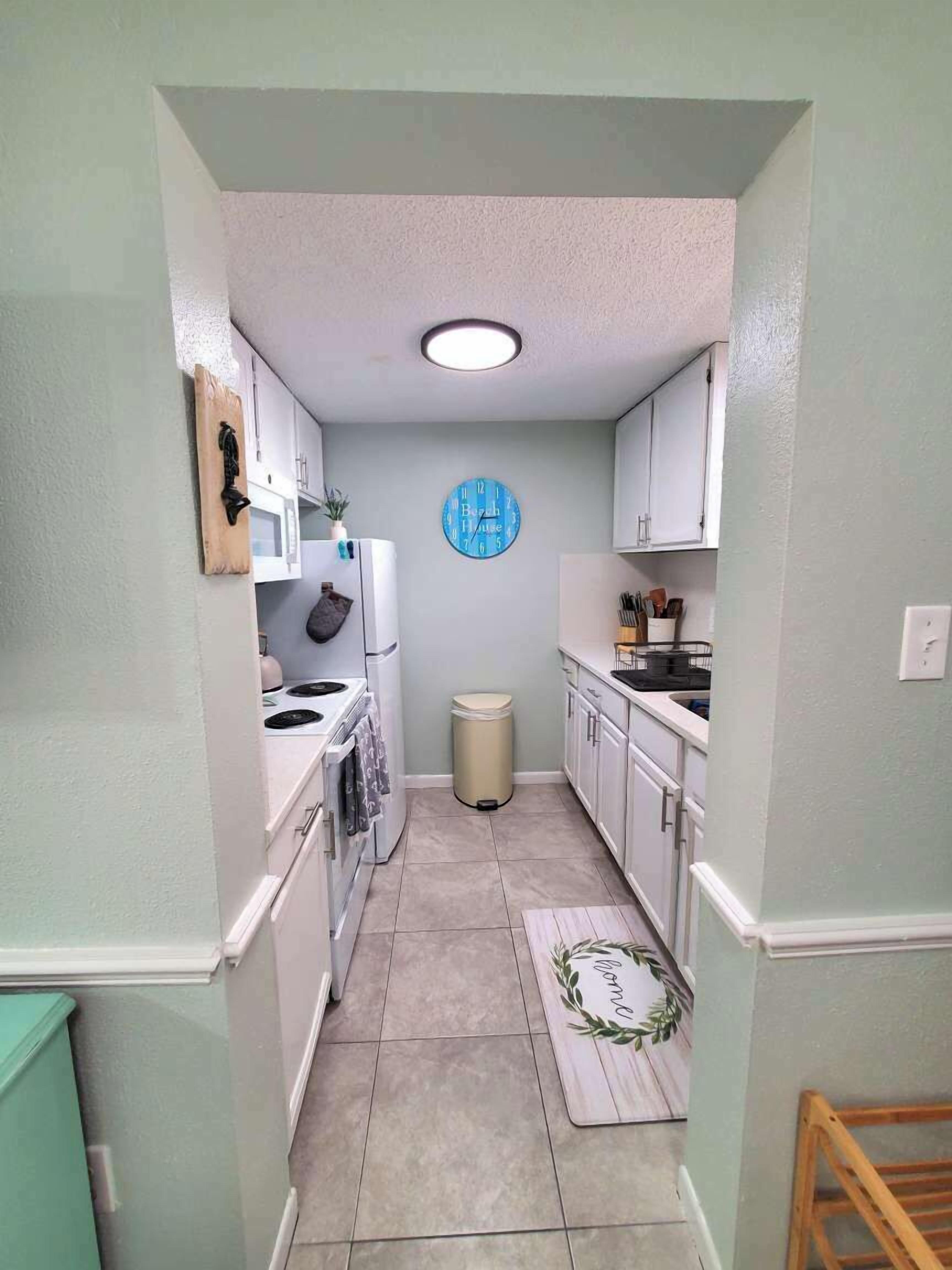 A narrow kitchen with white cabinets, a microwave, a stove, and a trash bin.