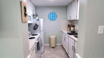 A narrow kitchen with white cabinets, a microwave, a stove, and a trash bin.