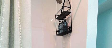 A shower with a hexagonal tile floor, a metal showerhead, and a black shelf with toiletries.