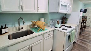 A kitchen with white cabinets, a stainless steel sink, a stove, and a microwave.