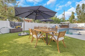 A backyard with a pool, a wooden table with chairs, and a large umbrella.