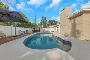 A swimming pool with a deck, lounge chairs, and a covered area.