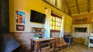 A rustic wooden interior with a fireplace, a television mounted on the wall, and a stone fireplace. - RECANTO DOS COMPADRES (Praia Grande)
