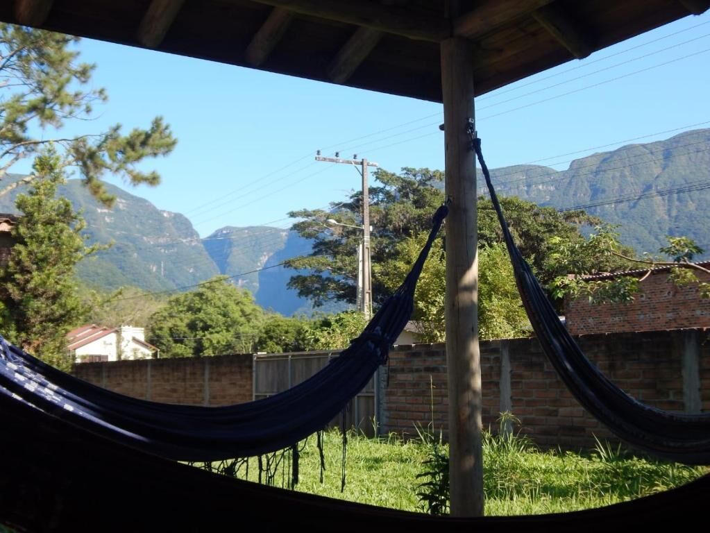 A hammock under a wooden structure with a view of mountains and a brick building in the background.