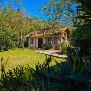 Uma casa rústica com telhado inclinado, rodeada por um gramado bem cuidado e folhagem densa.