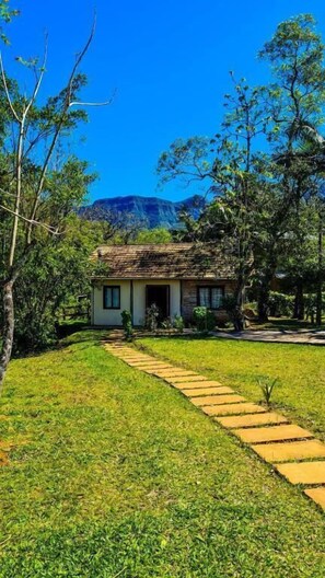 A single-story house with a thatched roof, surrounded by lush greenery and trees. - RECANTO DOS COMPADRES (Praia Grande)