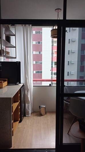 A small kitchenette with a window, a trash bin, and a view of a red building.