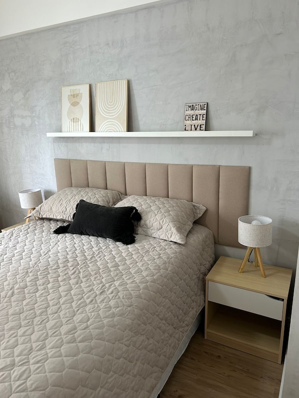 A modern bedroom with a large bed, a headboard, bedside tables with lamps, and decorative items on a shelf.