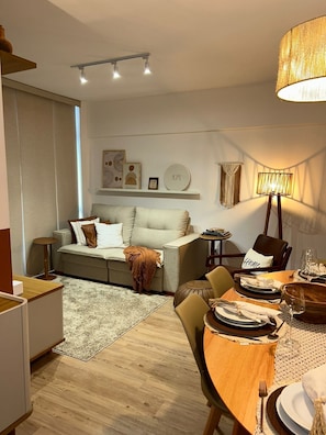 A modern living room with a sofa, a dining table set for two, and a lamp.