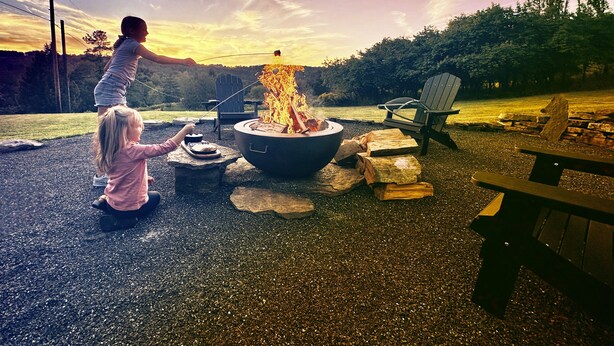A campsite with a fire pit, picnic table, and Adirondack chairs.