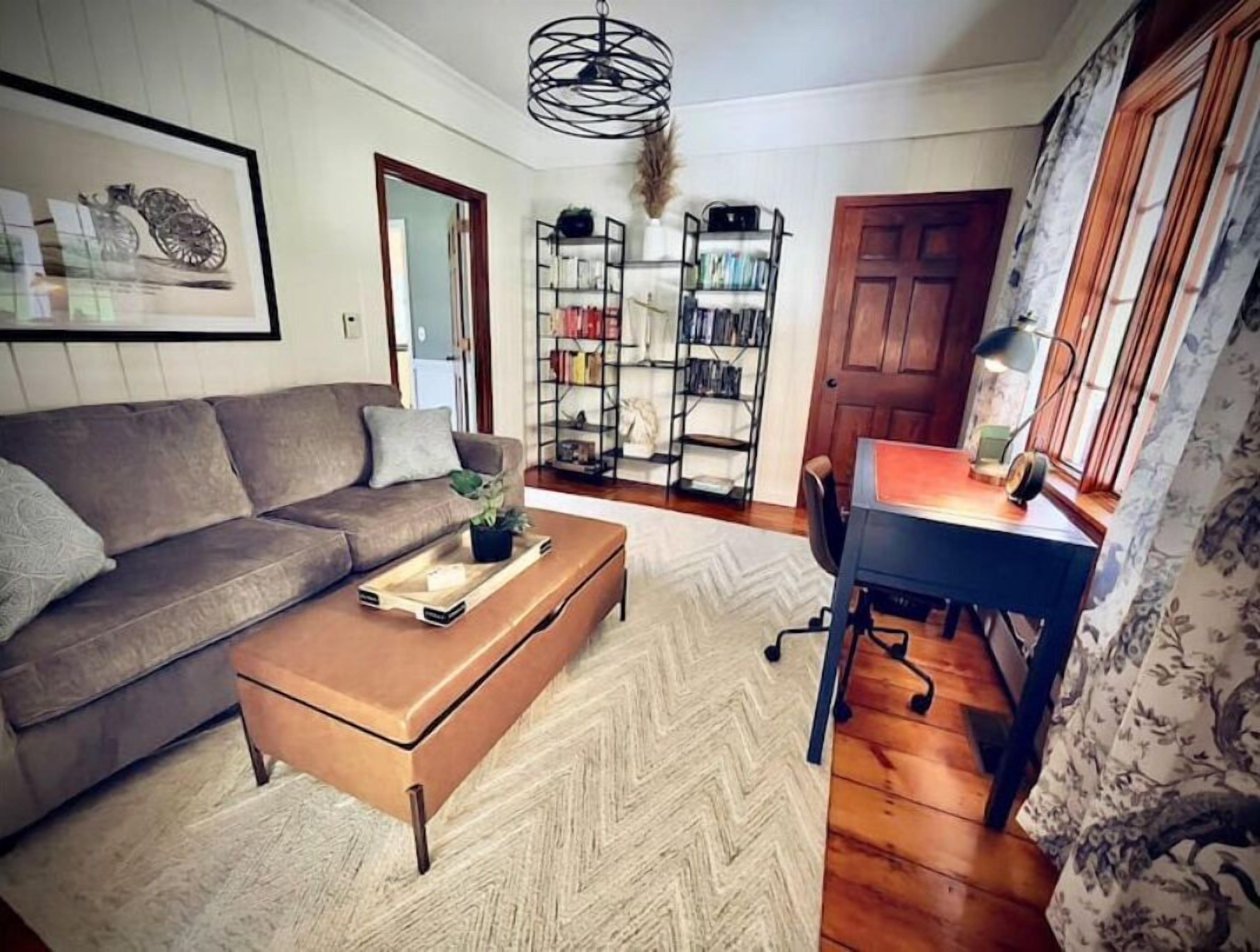 A living room with a sofa, a coffee table, a bookshelf, and a desk with a lamp.