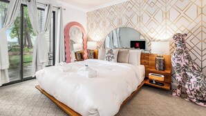 Une chambre d’hôtel avec un grand lit, une télévision, une table de chevet en bois et une vue à travers la porte vitrée.