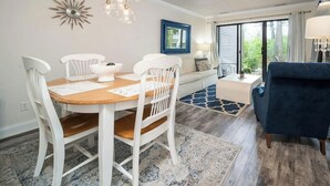Un coin repas avec une table en bois, des chaises blanches, un lustre et un mur d’accent bleu.
