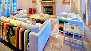 A spacious living room with a fireplace, a television mounted above it, and a large window with blinds. - Private 5 BDR Pet Friendly Mountain Villa w/ Jacuzzi minutes from Santa Fe (Rowe)