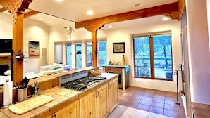 A spacious kitchen with wooden cabinetry, a large island, and a view of the outdoors through large windows. - Private 5 BDR Pet Friendly Mountain Villa w/ Jacuzzi minutes from Santa Fe (Rowe)