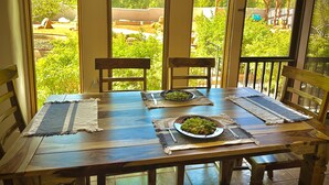 A wooden dining table with two chairs, set with placemats and plates of food, in a room with large windows overlooking a garden. - Private 5 BDR Pet Friendly Mountain Villa w/ Jacuzzi minutes from Santa Fe (Rowe)