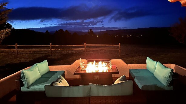An outdoor seating area with a fire pit and cushions, overlooking a landscape with distant lights. - Private 5 BDR Pet Friendly Mountain Villa w/ Jacuzzi minutes from Santa Fe (Rowe)