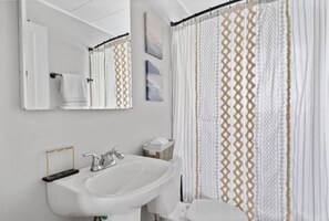 Un baño con un lavamanos blanco, un espejo y una cortina de ducha con diseño geométrico.