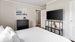 A bedroom with a bed, a dresser, a TV mounted on the wall, and two framed pictures on the wall. - Whole House in Bay View + Fenced-in Yard + Parking (Milwaukee)