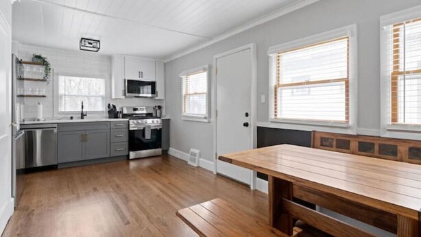 A modern kitchen with grey cabinets, stainless steel appliances, and a wooden dining table. - Whole House in Bay View + Fenced-in Yard + Parking (Milwaukee)