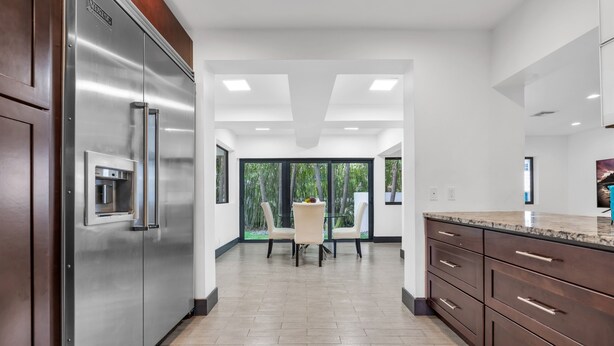 A modern kitchen with stainless steel appliances, wooden cabinets, and a large window offering a view of greenery. - 4BR Steps to Beach Home Private Pool, Hot Tub, BBQ (Fort Lauderdale)