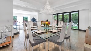 A modern dining area with a glass table, white chairs, and a chandelier. - 4BR Steps to Beach Home Private Pool, Hot Tub, BBQ (Fort Lauderdale)