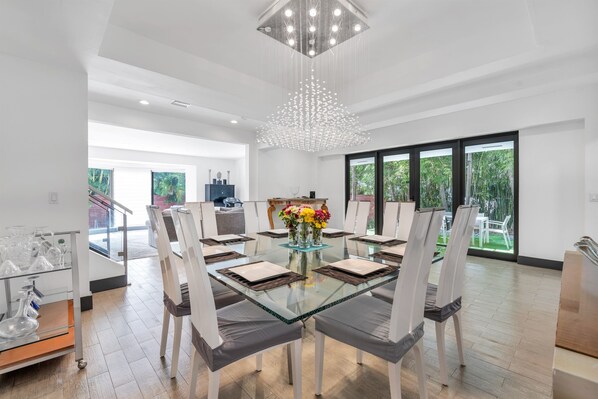 A modern dining area with a glass table, white chairs, and a chandelier.