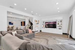 A modern living room with a grey sectional sofa, a large flat-screen TV, and a staircase leading to an upper level.
