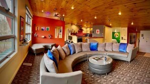A cozy living room with a curved sectional sofa, a round coffee table, and a kitchen in the background. - The Lookout (Galeton)