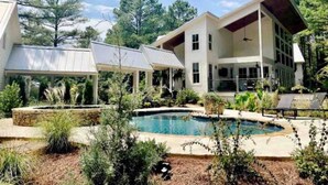 A modern house with a swimming pool, covered patio, and lush landscaping.