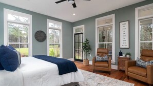 A bedroom with a bed, two chairs, a clock, a plant, and a motivational quote on the wall.