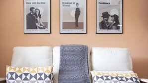 Ein Wohnzimmer mit einer Sofagarnitur, drei gerahmten Postern an der Wand und gemusterten Zierkissen.