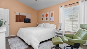 Ein Schlafzimmer mit einem Bett, einem grünen Sessel, einem Deckenventilator und Kunstwerken an der Wand.