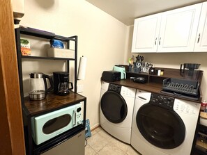 Une cuisine compacte équipée d’une machine à café, d’un grille-pain, d’un four à micro-ondes et d’un lave-linge.