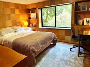 A bedroom with a bed, bedside table, lamp, and a desk with a chair.