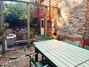 Une terrasse extérieure avec une table et des chaises, entourée d’un mur de briques et de verdure.