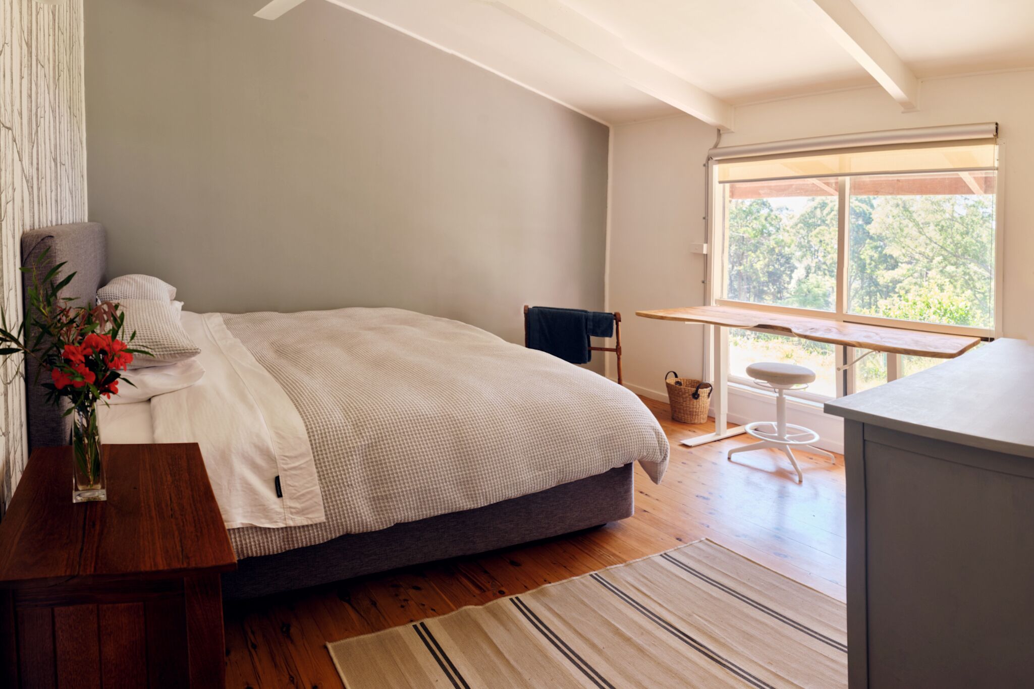 Une chambre à coucher avec un lit, un bureau, une chaise, une fenêtre et une vue sur les arbres.