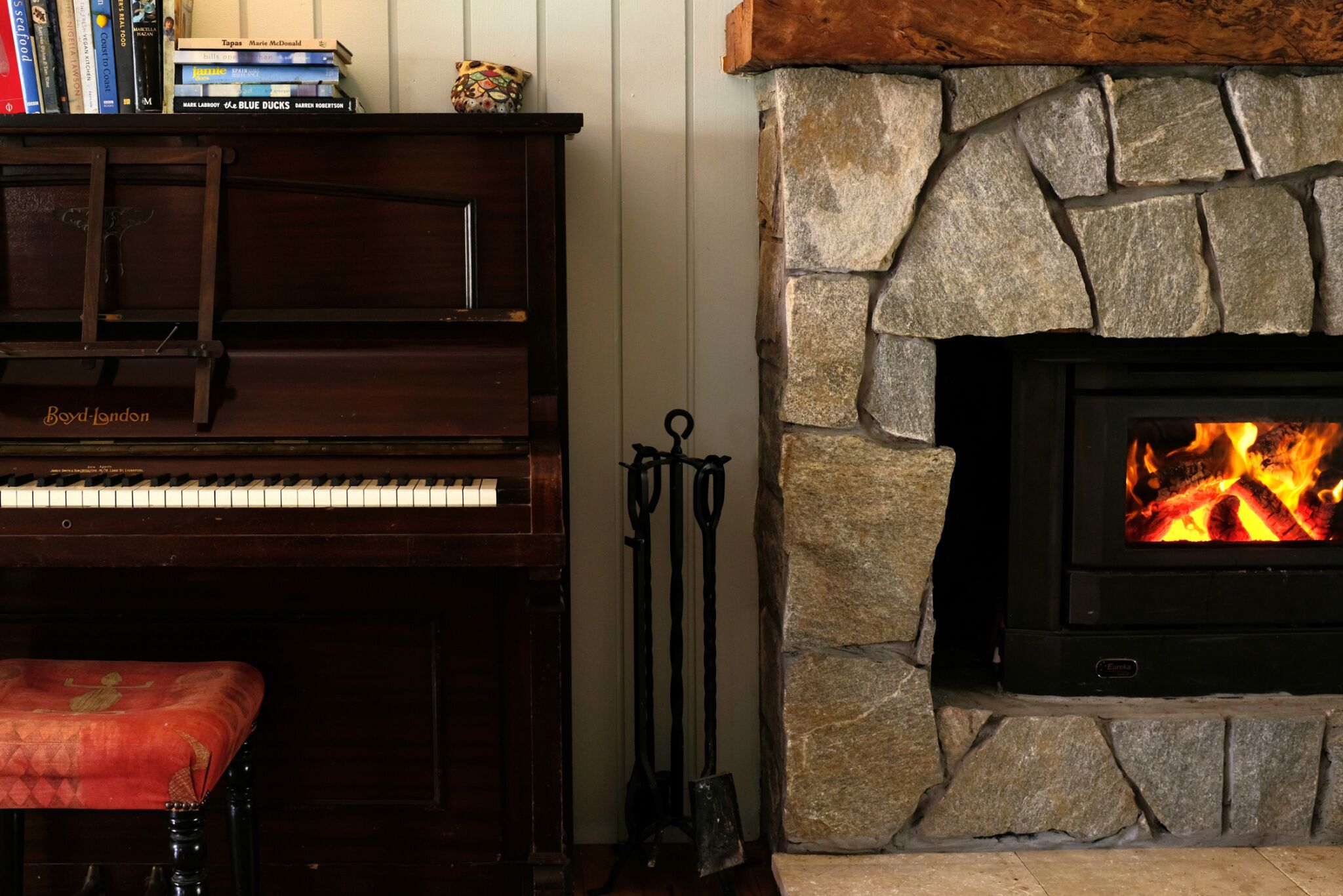 Um piano, uma lareira de pedra e uma pilha de livros.