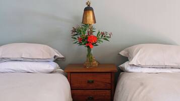 Une chambre avec deux lits, une table de chevet avec une lampe et un vase de fleurs, et un tiroir en bois.