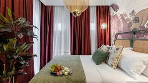 Une chambre d’hôtel avec un lit, une table à manger avec de la nourriture, des rideaux rouges et blancs, et une grande plante.