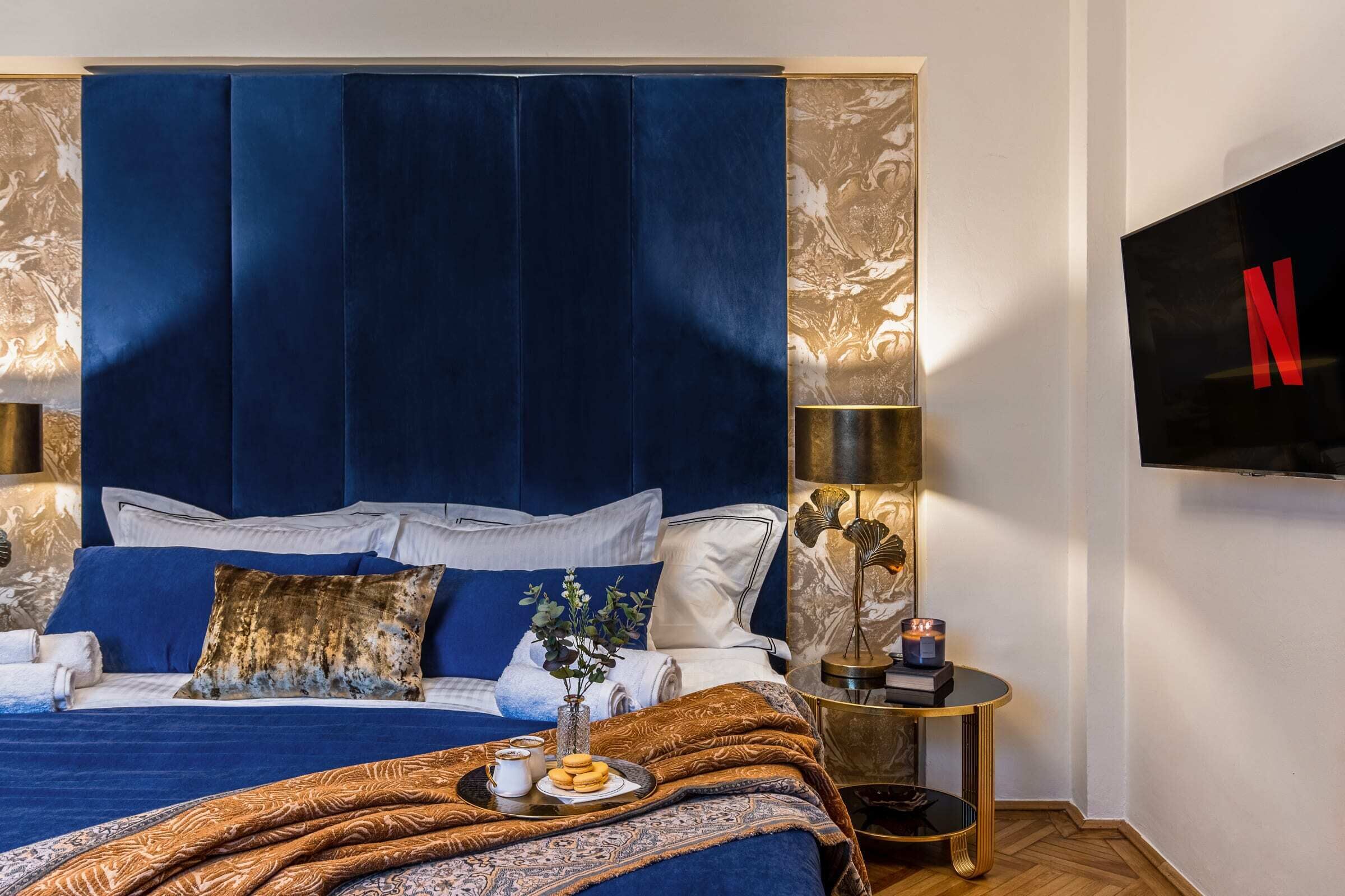 Quarto com cama grande, TV fixada na parede e mesa de cabeceira com abajur e um vaso.