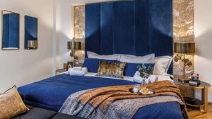 A modern bedroom with a large bed, blue bedding, and a decorative headboard. - Holt - The Great Gatsby (Bucharest)