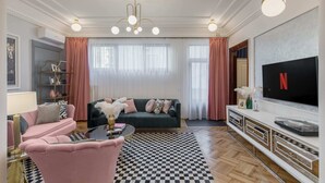 A modern living room with a checkered rug, a green sofa, a pink armchair, and a TV on the wall. - Holt - The Great Gatsby (Bucharest)