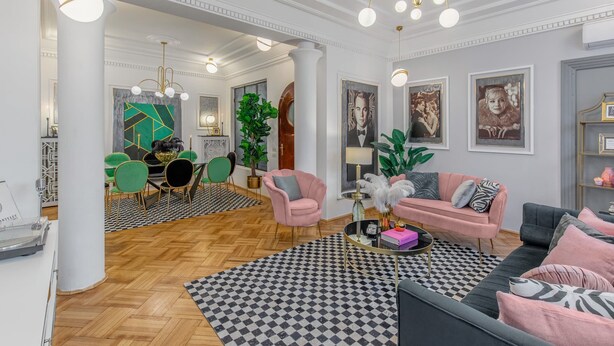 A spacious living area with a checkered rug, a black sofa, a pink armchair, and a dining area with green chairs and a wooden table. - Holt - The Great Gatsby (Bucharest)