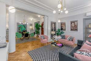 A spacious living area with a checkered rug, a black sofa, a pink armchair, and a dining area with green chairs and a wooden table. - Holt - The Great Gatsby (Bucharest)